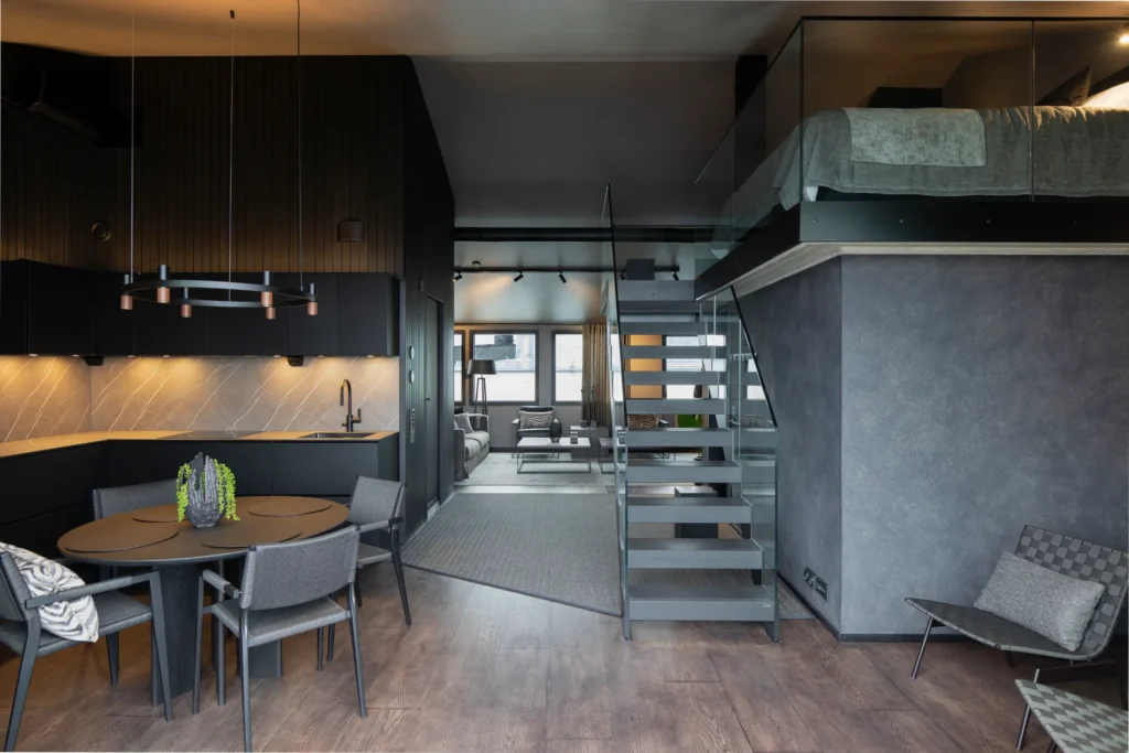 Keittiö ja ruokailutila yhtenäisenä kokonaisuutena, tumma keittiö ja design-portaat – sisustussuunnittelu